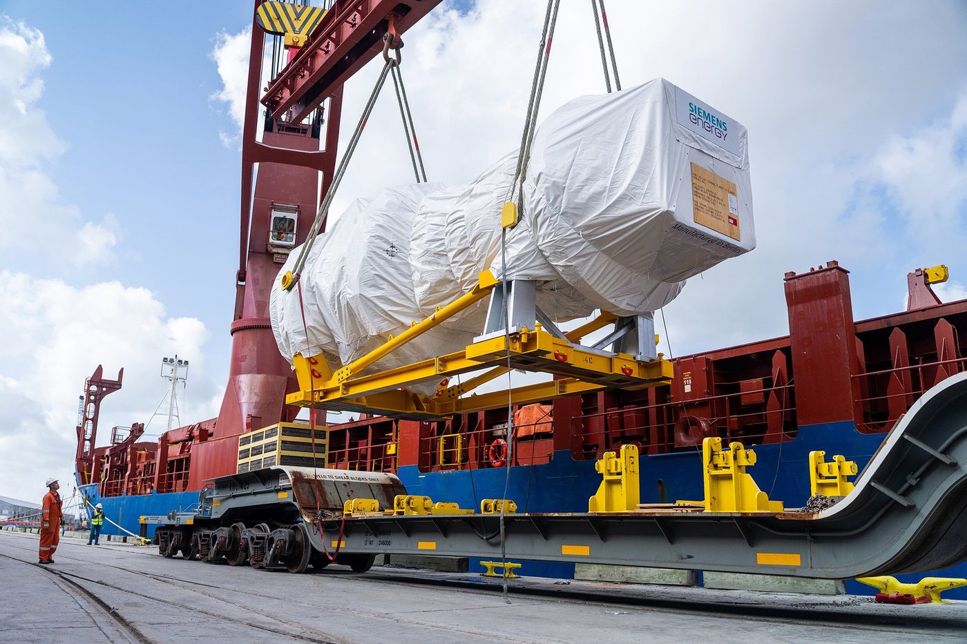 A wrapped Siemens Energy SGT6-5000F gas turbine on a self-propelled transporter beneath a red port crane at the Port of Houston